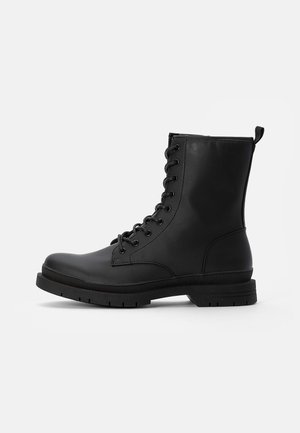 Mustad musta nahast lace-up pahkluu saapad, ümmarguse toe, kindla kummipõhjaga ja taga asuva tõmbeaugu abil, mis võimaldab mugavat selga panna.
