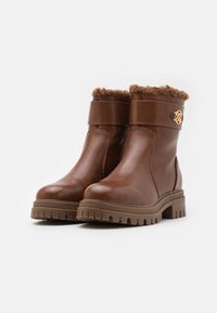 Bruna läderankelboots med faux fur trim, gummisula, rund tå och en dekorativ metallackcent på remmen.