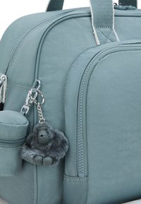 Light blue fabric bag with dual zippers, small side pocket, and a gray fuzzy gorilla keychain attached. Textured finish and sturdy straps.
