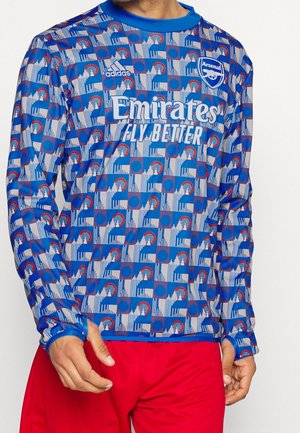 Blauwe patroon lange mouwen Arsenal voetbalshirt met "Emirates Fly Better" logo en Adidas branding, gedragen met rode korte broek.