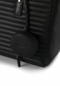 Ecke einer schwarzen Ledertasche mit strukturierter Oberfläche, horizontalen Nähten und einem runden, mit Reißverschluss versehenen Münzbeutel, der an einem Riemen hängt.