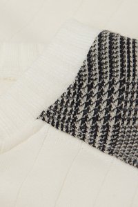 Tröjkrage med en krämfärgad ribbad textur och en svart och krämfärgad mönstrad tygpatch som framhäver varierande sticktekniker och färger.