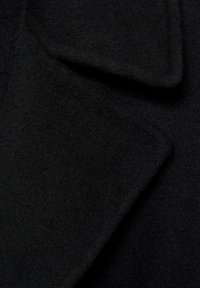 Tissu en laine noire présentant une surface douce et texturée avec un col et un revers pliés, mettant en valeur sa nature dense et chaude.