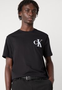 Svart bomull T-skjorte med korte ermer, rund hals, med en fremtredende hvit "cK" logo på brystet. Glatt tekstur, ledig passform.