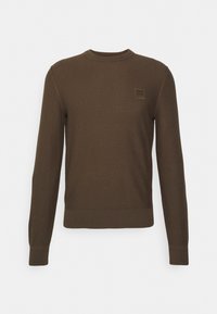 Brun stickad tröja med rund hals, långa ärmar och ribbad nederkant. Har ett texturerat mönster och en liten fyrkantig logotyp på bröstet.