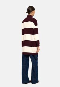 Bordowy i kremowy, pasiasty, oversize'owy sweter z wysokim kołnierzem; ma prążkowane mankiety i luźny krój, w połączeniu z szerokimi dżinsami.