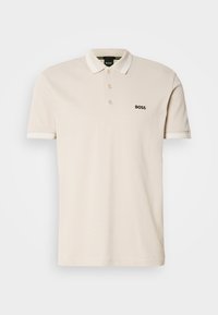 Polo beige à manches courtes avec col blanc et bordure de manches blanche, trois boutons, et logo noir "BOSS" sur la poitrine gauche.