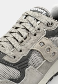 Baskets de sport gris clair, alliant des matériaux en mesh et en daim, avec des lacets texturés et un logo de marque distinctif sur la languette.