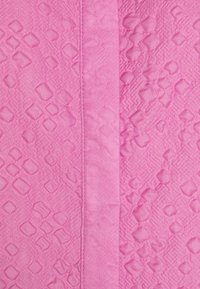 Tessuto rosa testurizzato caratterizzato da un mix di motivi geometrici in rilievo e sezioni lisce, con una cucitura piatta che corre verticalmente.