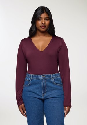 Body a maniche lunghe bordeaux con scollatura a V profonda, abbinato a jeans in denim blu a vita alta. Materiale liscio e design aderente.
