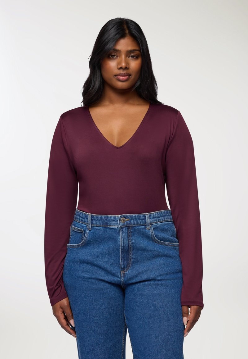 Bordowy bodysuit z długim rękawem i głębokim dekoltem w kształcie litery V, połączony z niebieskimi dżinsami z wysokim stanem. Gładki materiał i dopasowany krój.