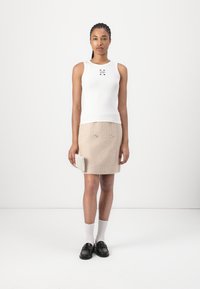 Weißes, geripptes Tanktop mit kleinem Logo; beiges Tweed-Minirock mit doppelten Vorderentaschen und silbernen Akzenten; Model hält eine strukturierte Clutch.