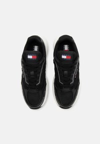 Par de zapatillas negras de Tommy Jeans con detalles de malla y cuero, suelas blancas, y logotipos de la marca en la lengüeta y el costado, vistas desde arriba.