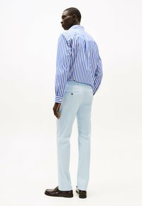 Camisa de botones a rayas azul y blanca, pantalones ligeros azul claro, zapatos marrones. Presenta mangas largas, pliegue trasero y detalle de bolsillo en la parte posterior.