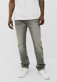 Jeans din denim gri cu o croială confortabilă, u�șor decolorate și cu detalii de cusătură la buzunare, asortați cu adidași albi.