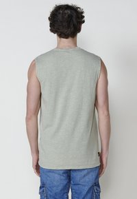 Bez piedurknēm, gaiši zaļa kokvilnas tank tops ar teksturētu apdari, kas piedāvā apaļu kakla izgriezumu un taisnu apakšmalu. Ievērojama plecu šuvju dizaina iezīme.