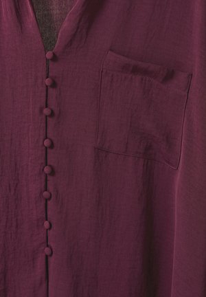 Blouse bordeaux avec un col en V, dotée d'une rangée de boutons ronds en tissu, d'une poche poitrine et d'un fini texturé semblable à du lin.