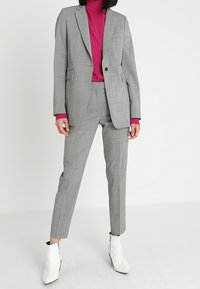 Šedý kostkovaný oblek s jedním knoflíkem a saka, doplněný vysokým magentovým topem. Modelka nosí bílé kotníkové boty pro kontrast.