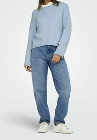 Jasnoniebieski sweter o fakturze z luźnym krojem, zestawiony ze średnioniebieskimi dżinsami. Model nosi białe sneakersy.