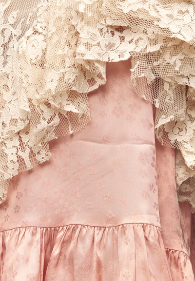 Ροζ σατέν ύφασμα με διακριτικό λουλουδάτο σχέδιο κάτω από στρώσεις κρεμ δαντέλας με λουλουδάτο και δίχτυ σχέδιο.