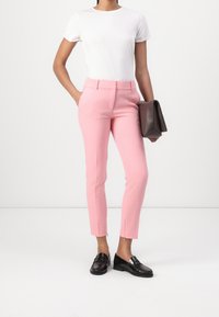 Pantalons ajustés roses clairs avec une coupe slim et des poches avant, associés à un t-shirt blanc et des mocassins noirs, tenant une pochette marron.