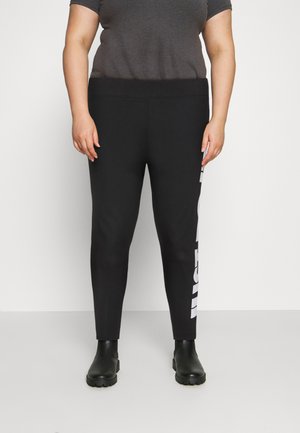 Μαύρες κολάν με λείο υφή, με λευκή κατακόρυφη εκτύπωση λογοτύπου στη αριστερή πλευρά. Συνδυάζονται με ένα σκούρο γκρι μπλουζάκι και μαύρες μπότες.