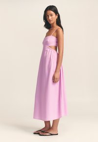 Abito maxi rosa senza maniche con design laterale a taglio, spalline sottili e vita elastica. Sandali neri piatti completano il look.