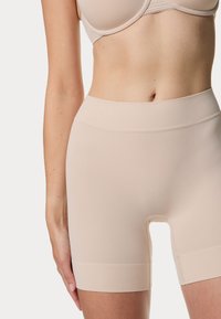 Beige compressiekorte broek met een hoge tailleband, een gladde textuur en een open uitsparing bij het kruis. Zacht en rekbaar materiaal.