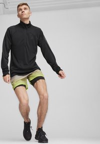 Musta puolipitkä vetoketjullinen yläosa, joka on yhdistetty vihreään gradienttiin lyhyet housut, joissa on musta vyötärö, ja ne on yhdistetty mustiin urheilukenkiin.