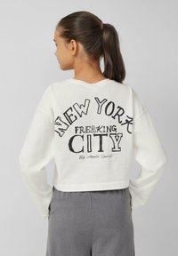 Witte cropped sweatshirt met een grafische print op de achterkant met "NEW YORK FREAKING CITY" in vetgedrukte zwarte tekst, lange mouwen en een ontspannen pasvorm.