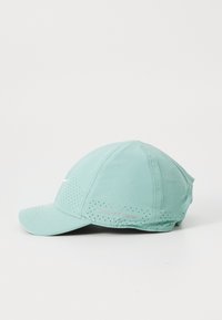 Lys grøn cap med en buet skygge, perforerede sider og en reflekterende "DRI-FIT ADV" detalje på siden. Lavet af åndbart stof.