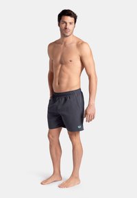 Bañador de hombre en gris oscuro, con cinturilla elástica, bolsillos laterales, costuras en contraste y logotipo en turquesa en la parte inferior de la pierna izquierda.