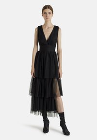 Robe noire sans manches avec un décolleté en V profond, jupe en tulle superposée et taille cintrée. Possède une texture douce et une silhouette fluide.