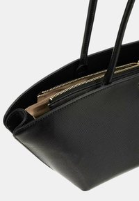 Sac fourre-tout noir structuré avec un extérieur texturé, deux longues poignées et un compartiment zippé doté d'une doublure neutre et d'un détail de marquage.