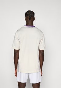 Helle Creme Fußballtrikot mit lila Akzenten. Verfügt über kurze Ärmel, einen Rundhalsausschnitt und den Schriftzug "FIORENTINA" auf dem oberen Rücken. Glatte Textur.