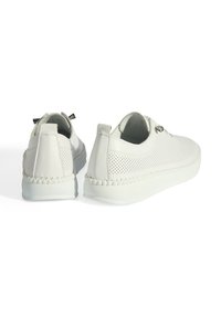 Baskets en cuir blanc avec des côtés perforés, semelles plates et couture décorative. Dotées d'une languette en boucle au talon pour un enfilage facile.