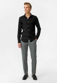 Zwarte button-up shirt met lange mouwen, gladde textuur, klassieke kraag, gecombineerd met lichtgrijze broeken en zwarte schoenen.