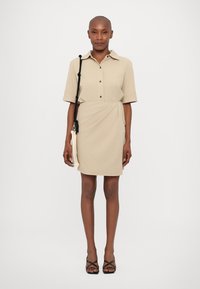Beige värvi särgikleid, mis on valmistatud pehmest kangast, omab nööpidega kraed, lühikesi varrukaid ja vööd, mis rõhutab ümbrise disaini.