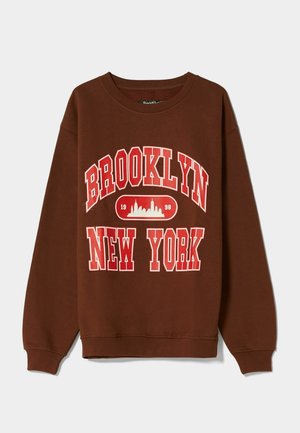 Brauner Sweatshirt mit rotem und weißem Schriftzug "Brooklyn New York" und rotem Skyline-Grafik mit der Jahreszahl 1998 auf der Brust, Rundhalsausschnitt und langen Ärmeln.