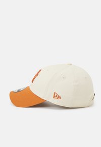 Cap with a cream fabric body and an orange brim. Features embroidered accents and a round top button. New Era logo on the side.