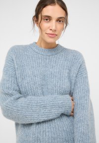 Šviesiai mėlynas, raukšlėtas megztinis su apvaliu iškirptimu ir ilgomis rankovėmis, pagamintas iš minkštos, purios medžiagos, pasižymintis laisvu siluetu.