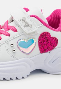 Weiße Sneaker mit pinken Akzenten, versehen mit einem glitzernden pinken Herz und einem glänzenden blauen Herzdesign an der Seite. Klettverschluss und strukturierte Sohle.