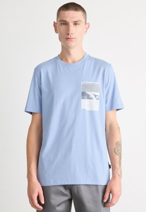 Lys blå bomulls t-skjorte med kort erm og et rektangulært grafisk lommedesign som viser et monokromt bilde og merkeetikett.