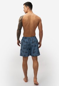 Heren zwemshorts, blauwe stof met een palmboomprint, elastische tailleband en achterzak. Geen extra versieringen of hardware.