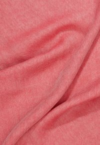 Gros plan sur un tissu rouge doux et plié montrant une fine texture tissée et des ombres subtiles formées par les plis.