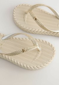 Goldene Glitzer flip-flops mit einer strukturierten beigen Sohle. Mit einem gewebten Design, flachen Riemen und einem kleinen Seestern-Accento in der Mitte.