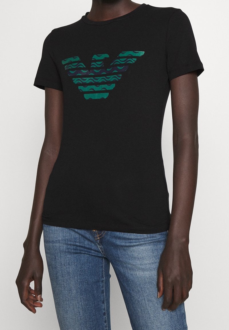 Černé bavlněné tričko s zeleno-modrým vzorovaným emblémem na hrudi. Krátké rukávy, kulatý výstřih a rovný lem.