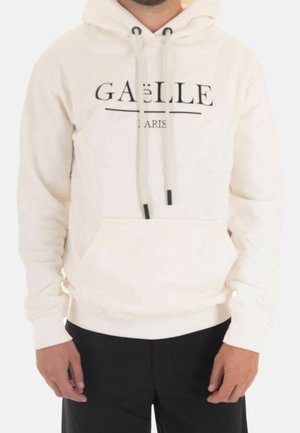 Sudadera color crema con un bolsillo frontal, capucha con cordón y texto negro "GAëLLE PARIS." Hecha de una tela suave y texturizada, con mangas largas.