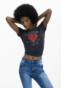 T-shirt nera corta con grafica di cuore rosso e scritta "Desigual", abbinata a jeans di jeans blu con ricamo floreale sulle tasche.