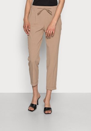 Pantalons beiges effilés avec une taille à cordon de serrage, poches latérales et poignets retroussés. Associés à des mules noires à bout ouvert. Texture lisse.